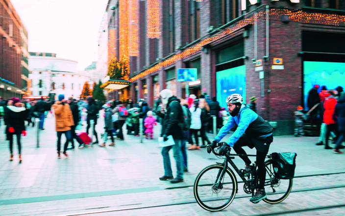 Talvinen kävelykatu Helsingissä, Stockmannin tavaratalon edessä. Paljon kansalaisia kulkemassa asioillaan jalan ja polkupyörällä.